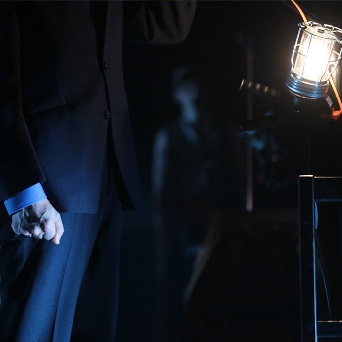 Musician on dark theatrical stage, single atmospheric light attached to microphone stand.
