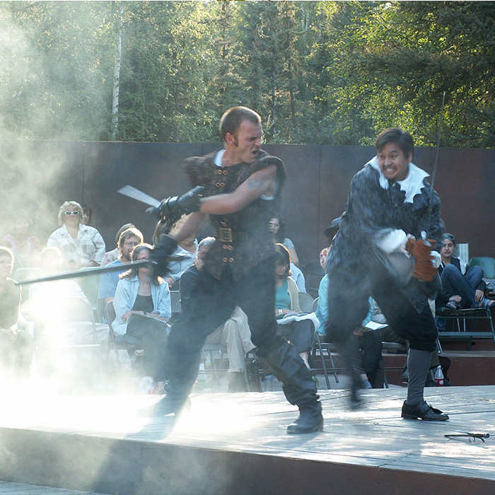 A dramatic scene from an epic production in Alaska. Sword fighting actors on stage with smoke effect.
