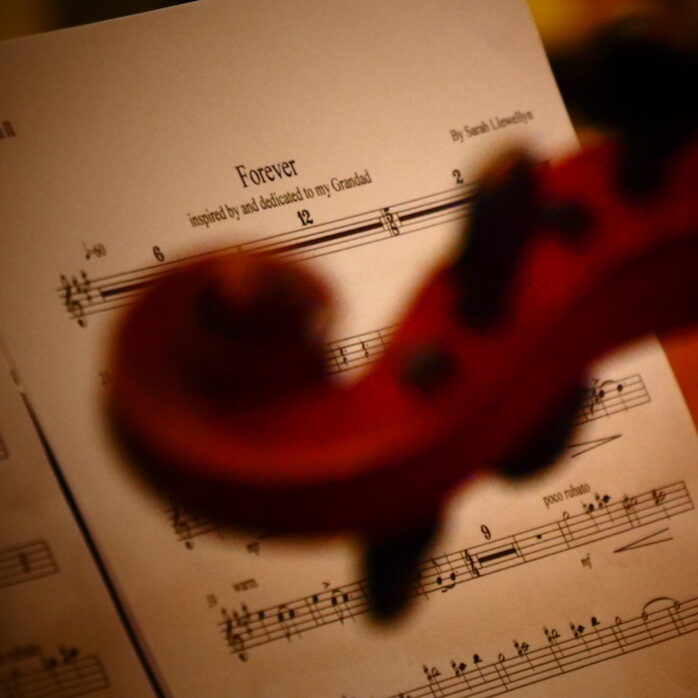 Out of focus violin head with notated music score of 'Forever' by Sarah Llewellyn, an original composition about love.