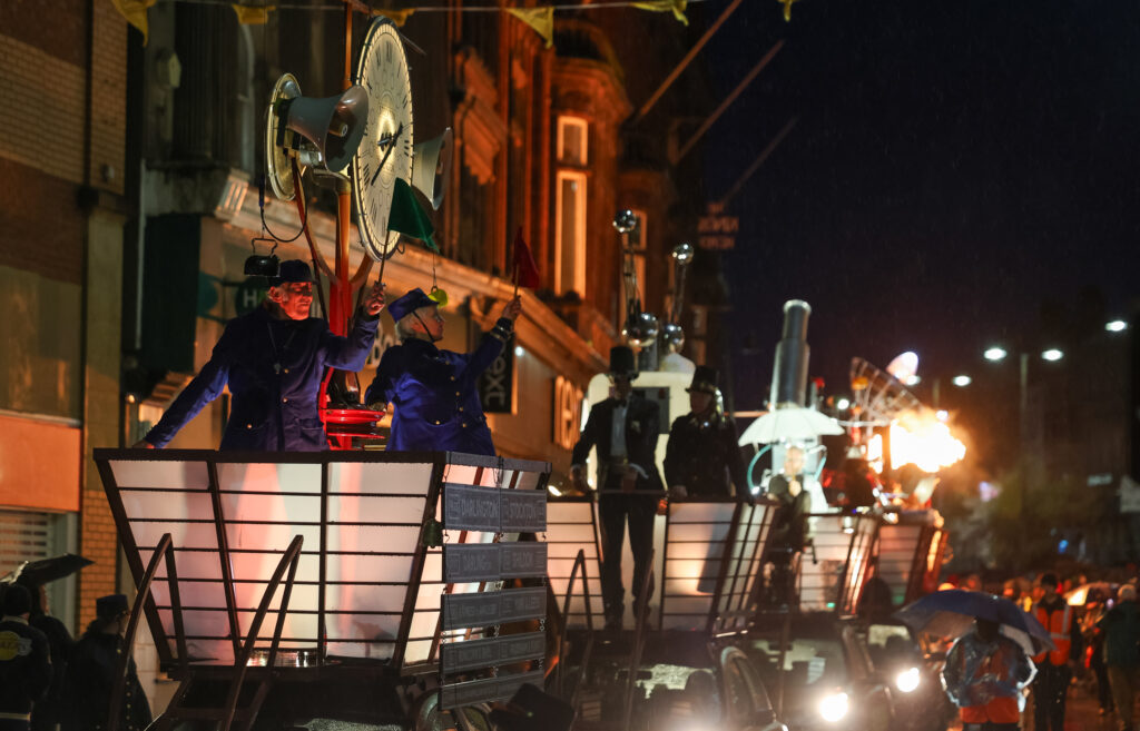 Photo from Ghost Train outdoor night parade in Darlington. Illuminated sculptures with performers atop nissan micra cars. Audience follow the procession.